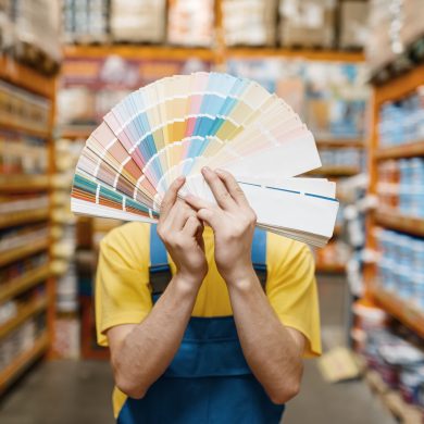 Male builder showing color palette in hardware store. Constructor in uniform look at the goods in diy shop, paint department